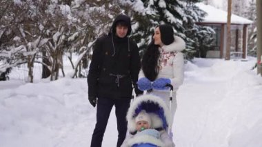 Sevgi dolu karı koca birlikte oğlu arabasındaki bebek şehir kış parkta bir yürüyüş sırasında şirin ve gülümseyen iletişim. Yürürken konuşmak güzel Çift.