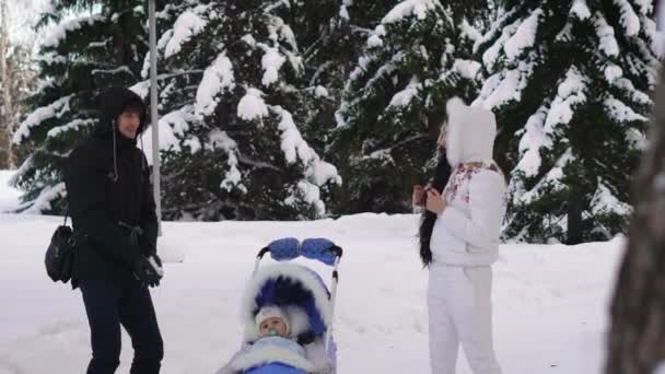 Homem feliz, vestido com um casaco preto, um capuz na cabeça, calças pretas, joga neve que voa para sua esposa. Uma mulher vestida com roupas brilhantes de inverno . — Vídeo de Stock