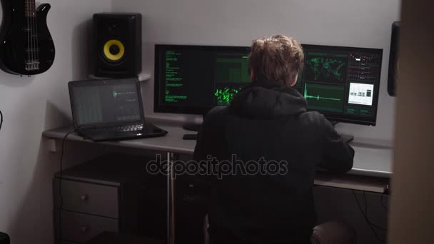Hacker verzamelt diverse computergegevens voor hacken database. Speciaal opgeleide jonge man die werkt voor meerdere beeldschermen en een laptop in een kleine kamer. — Stockvideo