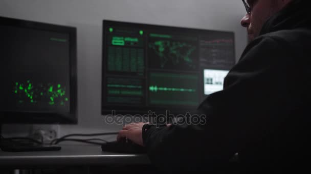 Sala de computadoras. En computadoras y teclado de escritorio. El hacker intenta entrar en información crítica. Un hombre con una chaqueta oscura y gafas recoge información usando el teclado es muy concentrado . — Vídeo de stock