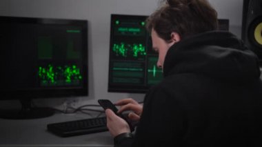 Yetişkin erkek siyah spor ceket Hacker, anız yüzünde, gizli bir sığınakta oturur ve siber saldırılar yapar. Smartphone, verileri dedi