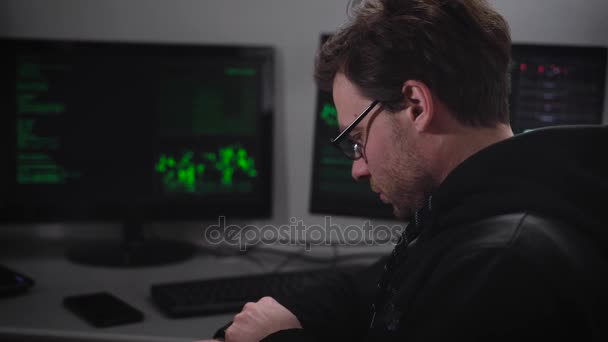 El hombre de la sala de ordenadores. Joven con gafas mirando de cerca su reloj de manzana, y también hace que ver cierta información. La habitación tiene dos computadoras, un ordenador portátil . — Vídeos de Stock