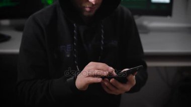 Hızlı bir şekilde gözlük ve ceket başlık giyen genç adam onun smartphone veri girin. Hacker kötü adam mobil teknoloji siber saldırılar sırasında bir yeraltı ofiste parasal kazanç için kullanır.