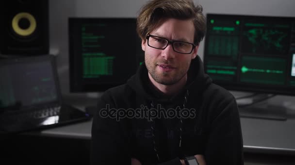 O homem de close-up preto. Sala de informática. Jovem especialista para hackear computadores em uma jaqueta preta com um olhar severo olhando para a câmera e sentado na posição fechada . — Vídeo de Stock