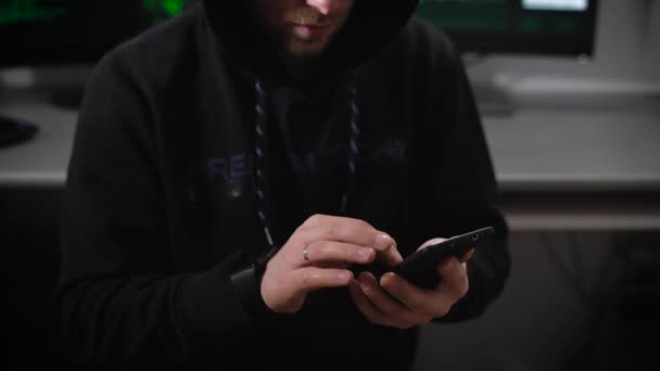 Der junge Mann mit Brille und Kapuze gibt schnell Daten in sein Smartphone ein. Hacker-Bösewicht nutzt mobile Technologie bei Cyber-Angriffen für Geldgewinn in einem unterirdischen Büro. — Stockvideo