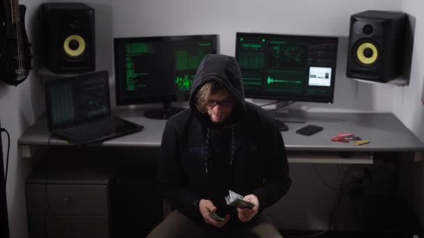 Vermummte Hacker in schwarzer Kleidung sitzen auf einem Stuhl im Raum und zählen Vorkasse für das Hacker-Netzwerk. nach der Überprüfung Geld Mann steckt es in die Tasche und wendet sich an den Computer, um Cyber-Kriminalität zu machen. — Stockvideo