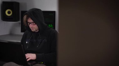 Onun natbukom oturma ve programlar içinde kesmek meşgul renk kayushonom ile siyah bir hoodie memnun Hacker. Arka planda uydular izleyebileceğiniz birkaç bilgisayar ekranları olduğunu