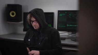 Bir hacker bilgisayar odasında. Gözlük ve yabancı üsler bilgileri girmeye çalışırken bir yandan laptop olan adam. Çoğu bilgisayarlarla donatılmıştır.