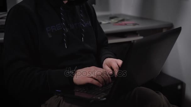 El joven hacker en una computadora portátil crea un programa de virus para ataques cibernéticos en el servidor bancario. Hombre con una chaqueta oscura y gafas escribiendo rápidamente en el teclado y luego sonríe . — Vídeo de stock