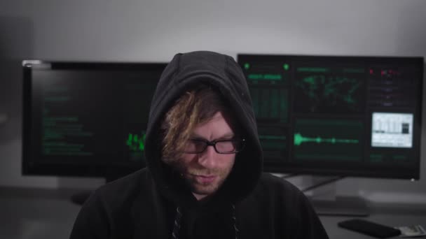 Close up of a spy with smartwatch sitting and using laptop with computer monitors behind him. Criminal man in eyeglasses typing quickly and trying to gain unauthorized access to important information. — Stock Video