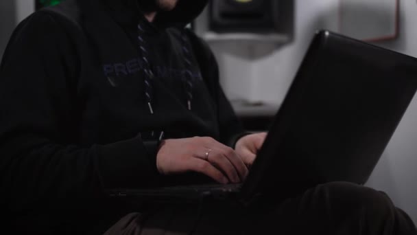 El hombre astuto, vestido con una chaqueta negra y una capucha en la cabeza termina de imprimir texto en el monitor de la computadora y cierra la tapa. Sonríe medio labios, golpea sus ojos . — Vídeos de Stock