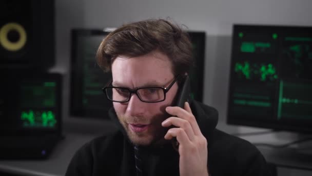 Jonge It-professional praten op zijn mobiele telefoon tegen een achtergrond-computers die werken met E-informatie in klein kantoor. — Stockvideo