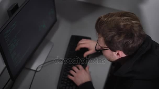 Sala de ordenadores subterráneos. Un hacker que usa software especial intenta descifrar la información importante. Un hombre con una chaqueta oscura y gafas recoge información usando el teclado es muy concentrado . — Vídeos de Stock