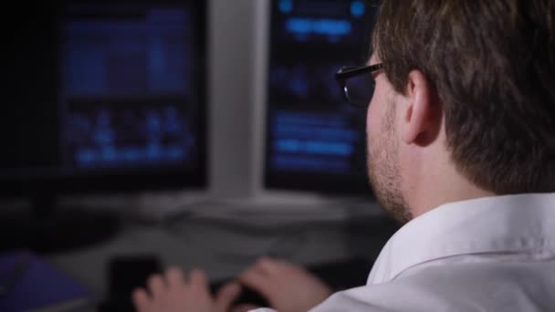 Vue de dos d'un jeune homme d'affaires avec smartwatch sur la main travaillant à son bureau dans le bureau. Image des mains d'un gestionnaire assis devant les écrans d'ordinateur et tapant sur le clavier . — Video