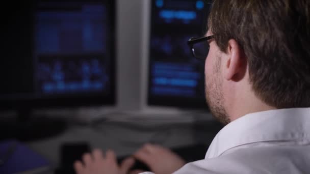 Rückansicht eines jungen Geschäftsmannes mit Smartwatch an der Hand, der an seinem Schreibtisch im Büro arbeitet. Bild der Hände eines Managers, der vor Computermonitoren sitzt und auf der Tastatur tippt. — Stockvideo