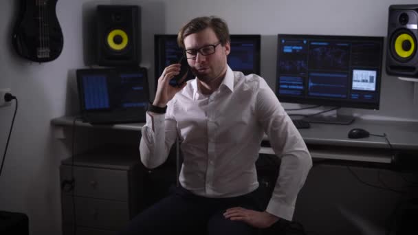 Experienced software developer smiling talking on his smartphone while computers on the background to handle a large number of E-information. Portable mobile communication in everyday life. — Stock Video