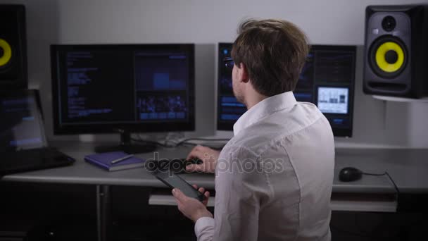 Υπόγεια οργάνωση. Σε ένα πίνακα υπολογιστές. Το άτομο σε ένα ανοιχτό πουκάμισο και βαθμούς βλέμματα στο smartphone, το άρθρο προσπαθεί να κατανοήσει πληροφορίες — Αρχείο Βίντεο