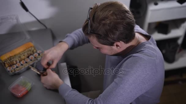 Computer room. The programmer during a lunch. The man is hungry and has decided to have a bite. On a table of sushi. The young guy opens sauce and packing with wasabi and ginger. — Stock Video