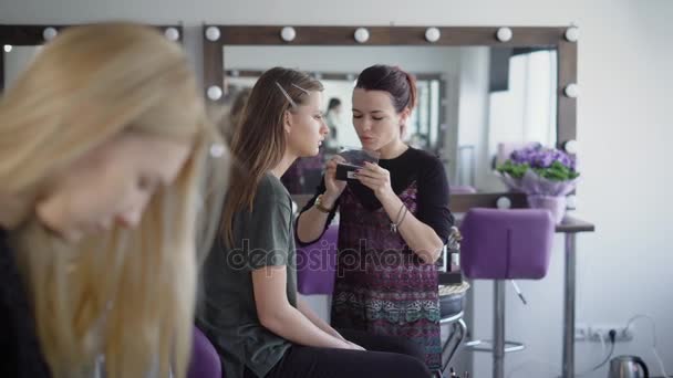 Estudio de belleza. El maestro en el maquillaje entrena al estudiante para la final. El maquillador pega pestañas falsas en los párpados de los clientes . — Vídeo de stock