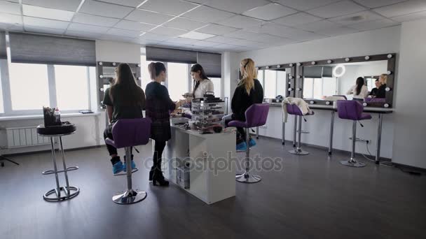 Interior of luxury beauty salon with two professional experts and two female models sitting. Professional visagistes are working with young girls applying new techniques of make-up. — Stock Video