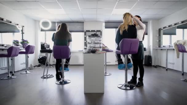 Interior de salón de belleza de lujo con expertos profesionales y modelos femeninos sentados. Vista posterior de las niñas que trabajan como modelos. Visagistas profesionales que aplican cosméticos demostrando nuevas técnicas . — Vídeos de Stock