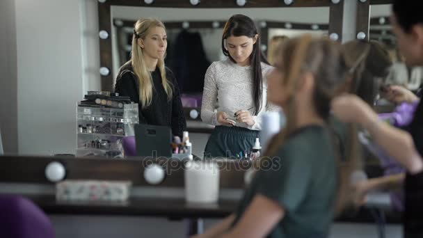 Nous pouvons voir deux maîtres, qui font leur travail dans le vestiaire. On essuie le pinceau avant d'appliquer le blusher, le second homme redresse ses cheveux au premier plan pour créer des coiffures — Video