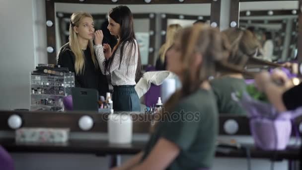 Twee vriendinnen in de schoonheidssalon. Meisjes voorbereiden een feest. De make-up artiest doet een make-up aan de blonde vrouw. Studio van schoonheid erg gezellig — Stockvideo