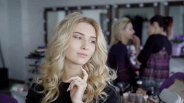Güzel sarışın kadın ile uzun kıvırcık saç ve stil makyaj seductively kameraya poz. Güzellik Salonu bir sandalyede oturan büyüleyici gözlü model.