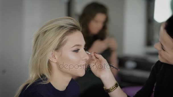 Close up. The master in a make-up prepares model for display. The girl puts with a brush of eye shadow. Smooth tone of the face, natural lips are very fashionable in this season. — Stock Video