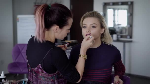 Visagiste artista en un apuro para terminar el maquillaje increíble para una actriz de cine muy famosa. Mujer joven con el pelo teñido con un lápiz labial caro en su trabajo. Industria de la moda dentro . — Vídeos de Stock