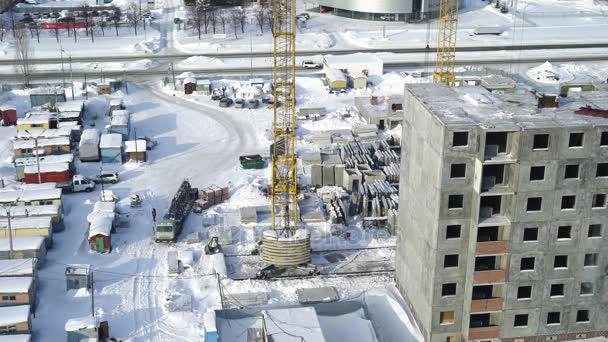 Μια μεγάλη κατασκευή γερανός μεταφέρει μια τσιμεντένια πλάκα κοντά στο Ημιτελές κτίριο κατά τη διάρκεια του χειμώνα. Η θέα από τα ύψη για την διαδικασία κατασκευής πολυώροφα κτίρια στη μικρή πόλη. — Αρχείο Βίντεο