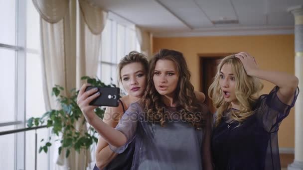 Three friends fool around in front of the camera, showing a fashionable pose to look better in pictures. They have a stylish hairstyle and natural, make-up, suitable for any event - wedding, birthday — Stock Video