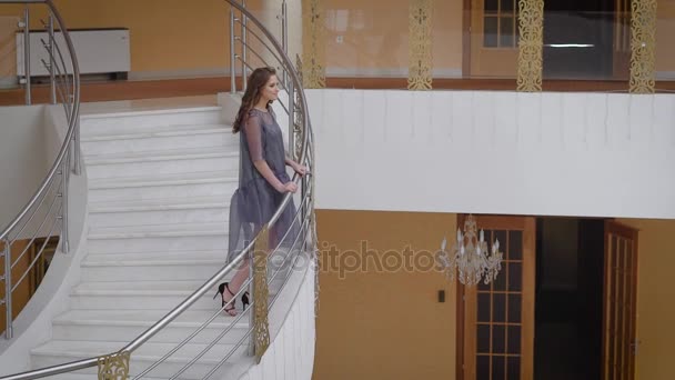 Φουαγιέ της αίθουσας smart. Τεράστια σκάλες, μαρμάρινο δάπεδο, όμορφους πολυελαίους. Το μοντέλο κορίτσι θέτει σε μια σκάλα. Το ξανθό κορίτσι σε ένα φόρεμα μεσαίου μήκους και ψηλά τακούνια. — Αρχείο Βίντεο
