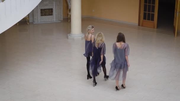 音乐厅的走廊。三个女朋友走。穿着漂亮的连衣裙的女孩走到出口。在大厅里漂亮的吊灯、 椅子和椅子，在墙上的壁炉. — 图库视频影像