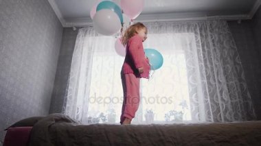 Mutlu küçük kız odasında yatakta hava balonları onun elinde avuç pencere atlama ve kameraya bakıyor. Küçük kadın çocuk mutlu kanepede dönüyor.