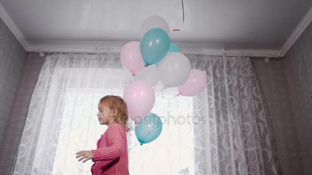 Dulce chica con el pelo rubio de pie en la cama de sus padres jugando con globos llenos de helio, pero una bola blanca voló y la chica salta alegremente para atraparlo — Vídeos de Stock
