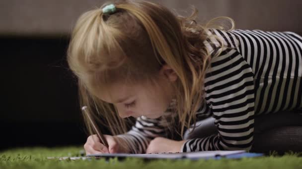 Close up of beautiful little girl in striped pullover drawing with brown pencil in nursery. Small princess is playing by painting the pattern with dark soft-tip pen. Cute child is spending her time at — Stock Video