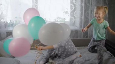 Mutlu aile evde yatakta oynuyor Başlarken pijama partisi. Ablası bir buhch renkli hava balon tutuyor ve küçük kız mutlu onu yakalamaya çalışıyor atlıyor.