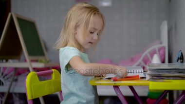 Küçük kız kalem masada oturan Studio ile resmi çiziyor. Farklı renkler yumuşak uçlu kalemler ile boyamak küçük çocuk öğrenme. Şirin çocuk desen zevk ile crayoning.