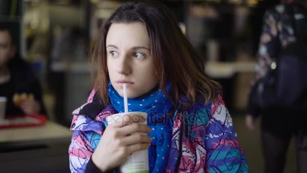 La chica corrió a la cafetería de la calle, que rápidamente comer. La morena se sienta en una chaqueta deportiva y bebe un refresco en un restaurante de comida rápida . — Vídeos de Stock