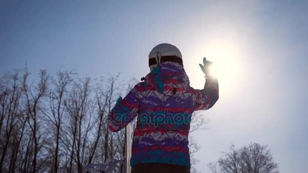 Quadro atmosférico, o conceito de sonhos e alegria do dia. Uma menina snowboarder pega um sol brilhante com a mão. Um dia de inverno claro nas montanhas — Vídeo de Stock