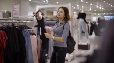 Genç, güzel küçük bir kız bir süpermarkette giysiler seçer. Kendisi için yeni bir gardrop bulmak için butik kız girdi.