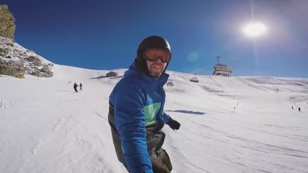 Narciarstwo w Alpach w zimie. Człowiek jest toczenia na snowboardzie na zaśnieżone szlaki górskiego kurortu. Facet zdejmuje sobie na dodatek aparat fotograficzny. — Wideo stockowe