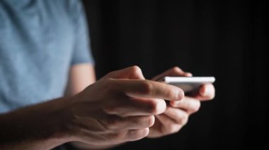 Kavramı, dijital online yaşam ve sosyal ağlar. Bir t-shirt bir işadamı onun smartphone onun hesapları görüntülemek için kullanır. Etkileyici atış, karanlık bir odada bir adam şık bir telefon tutarak