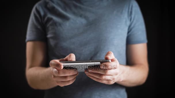 Conceito, vida online digital e redes sociais. Um homem de negócios em uma camiseta usa seu smartphone para ver suas contas. Tiro expressivo, um homem em um quarto escuro, segurando um telefone elegante — Vídeo de Stock