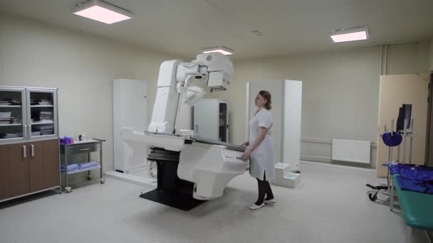 Nueva oficina médica moderna con varios equipos electrónicos en el interior. Una doctora ajusta la máquina de rayos X para trabajar con el paciente. Aparato universal moderno — Vídeos de Stock