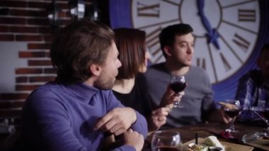 Bir masada aperatifler ve şarap ile modern bir restoranda çekici gençlerin bir grup. Erkekler ve kızlar kırmızı şarap içmek ve atıştırmalık yiyin. Arkadaşları başarılı sözleşme veya doğum günü kutlaması.