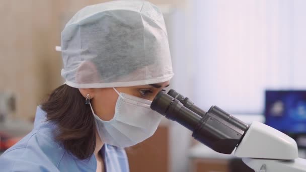 Close-up tiro do rosto de uma mulher que olha através de um microscópio, a fim de verificar um pacientes exames laboratoriais para fazer uma anamnese — Vídeo de Stock