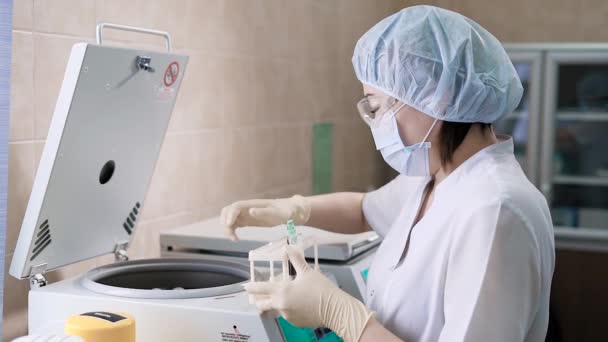 Close-up tiro de uma jovem mulher que está vestida com um manto branco e luvas, uma enfermeira coloca tubos de ensaio com sangue em um aparelho de centrífuga moderna — Vídeo de Stock