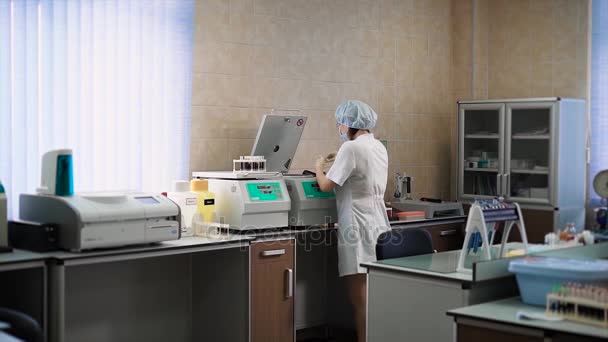 Лікар в клініці в білому пальто, який знаходиться в лабораторній кімнаті, розміщує аналізи крові в центрифужному апараті для якісного аналізу рівня плазми, сироватки, сечовини — стокове відео